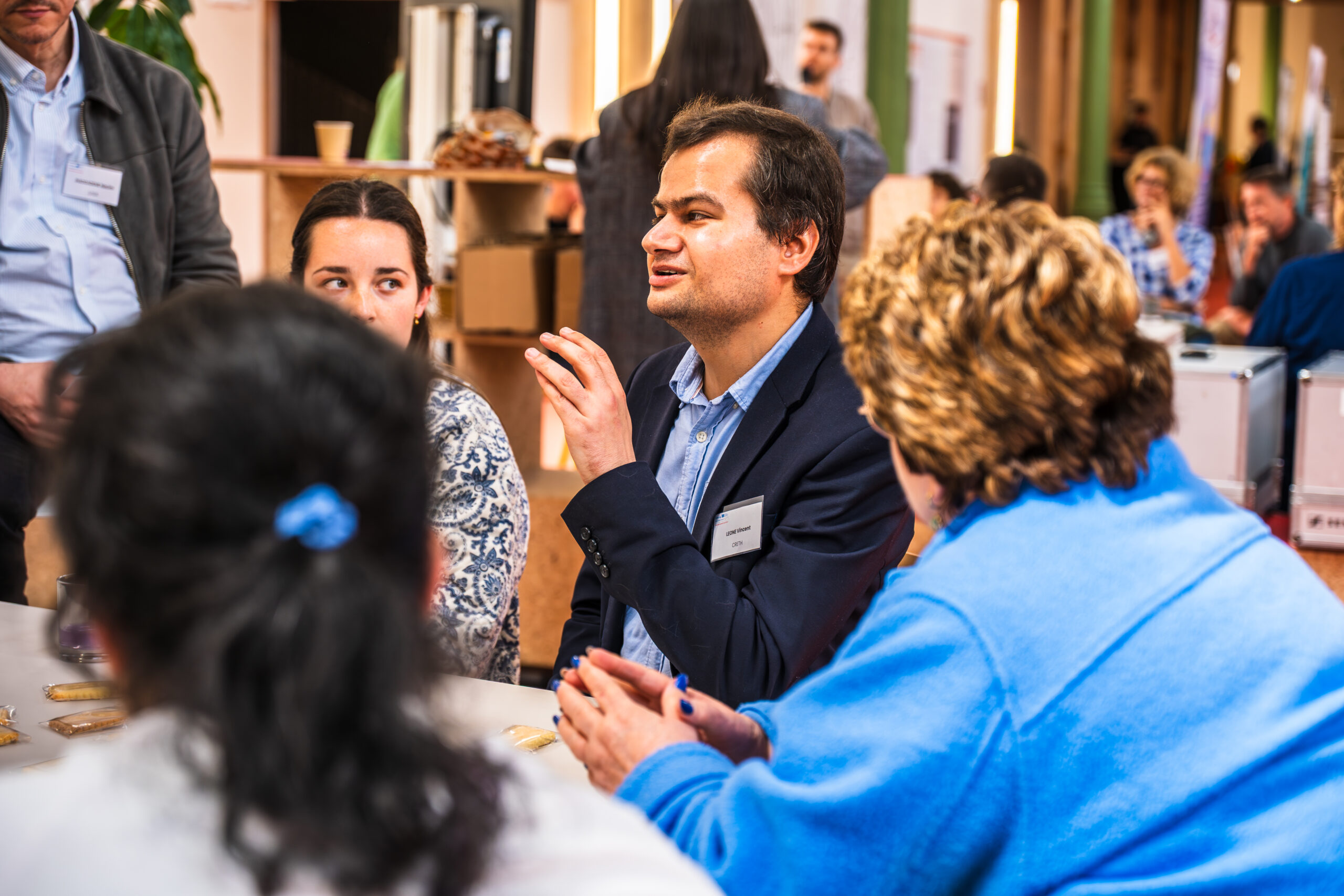 Vincent Léone en costume bleu discute avec des participants attablés, dans une ambiance conviviale avec des verres et des collations.