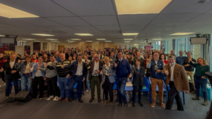 Photo de groupe prise lors de la cérémonie de remise des Prix de l’Excellence Handi Tech 2026 à la French Tech Lille. Un grand nombre de participants, debout dans une salle moderne avec des chaises bleues et un écran en arrière-plan, lèvent les pouces en signe de célébration. Plusieurs personnes au premier rang tiennent des trophées dorés en forme de silhouette en fauteuil roulant, symbolisant leur reconnaissance dans le domaine de l’innovation et de l’accessibilité. L’ambiance est joyeuse et collaborative, reflétant l’engagement des lauréats et des acteurs pour un tourisme et une technologie inclusifs.
