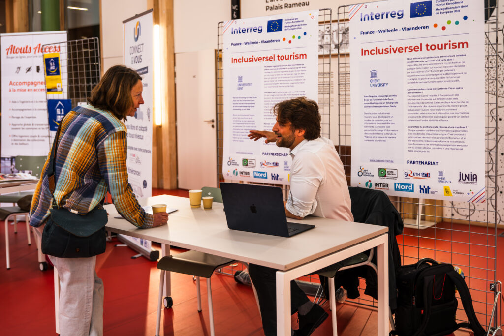 Un intervenant échange avec une participante devant les panneaux d'information du projet et de Ghent University.