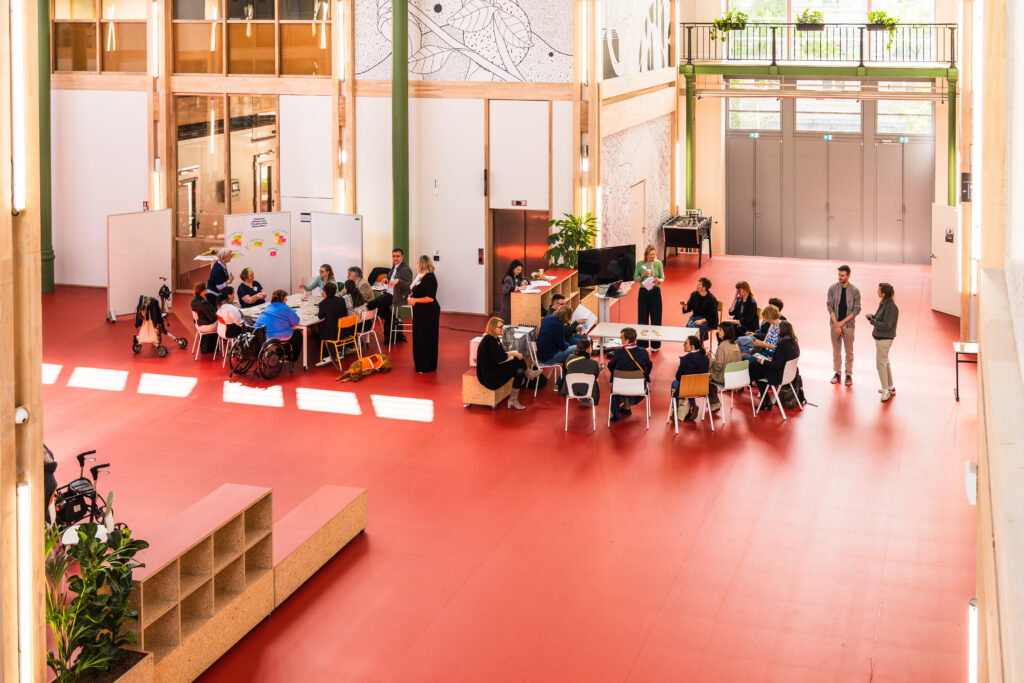 Vue plongeante sur les groupes de travail répartis dans la grande halle lumineuse.