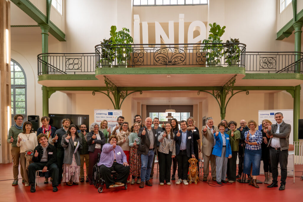 Photo de groupe réunissant les participants, intervenants et un chien guide posant avec les pouces levés dans la halle du Palais Rameau.